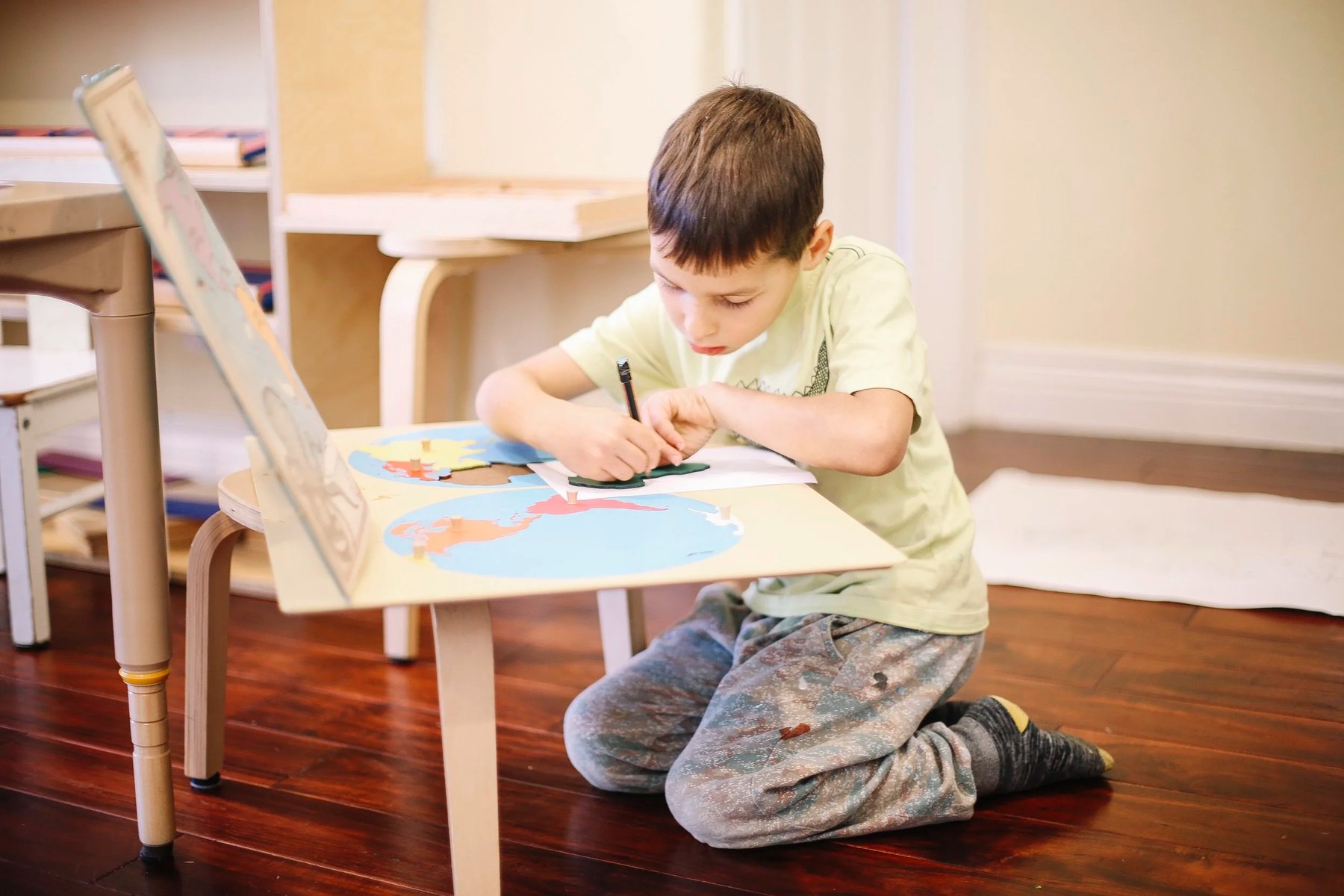 Child tracing a Montessori puzzle map piece during elementary geography work