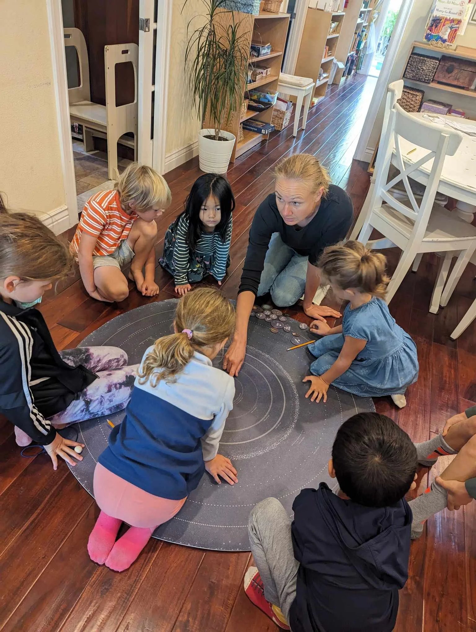 A guide leads six children seated around a large circular work mat for a cosmic or timeline presentation in the classroom